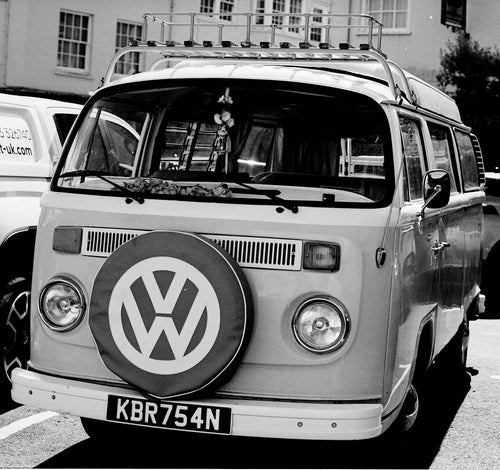 Vintage Volkswagen van with a spare tire cover on a street.