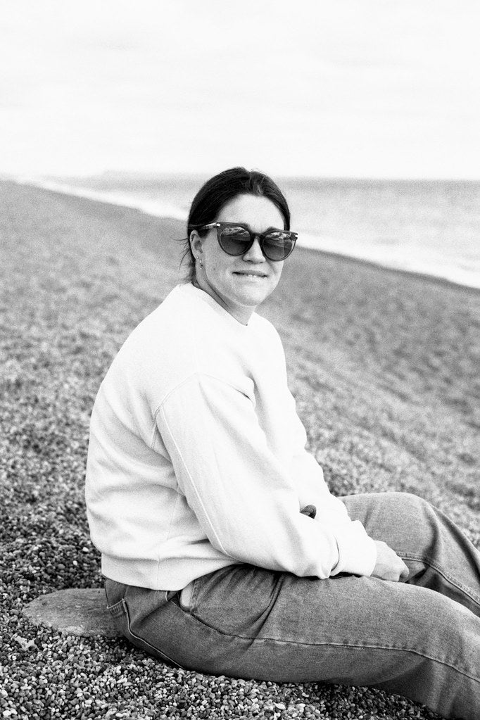 Person sitting on a beach wearing sunglasses and a light-colored sweater.