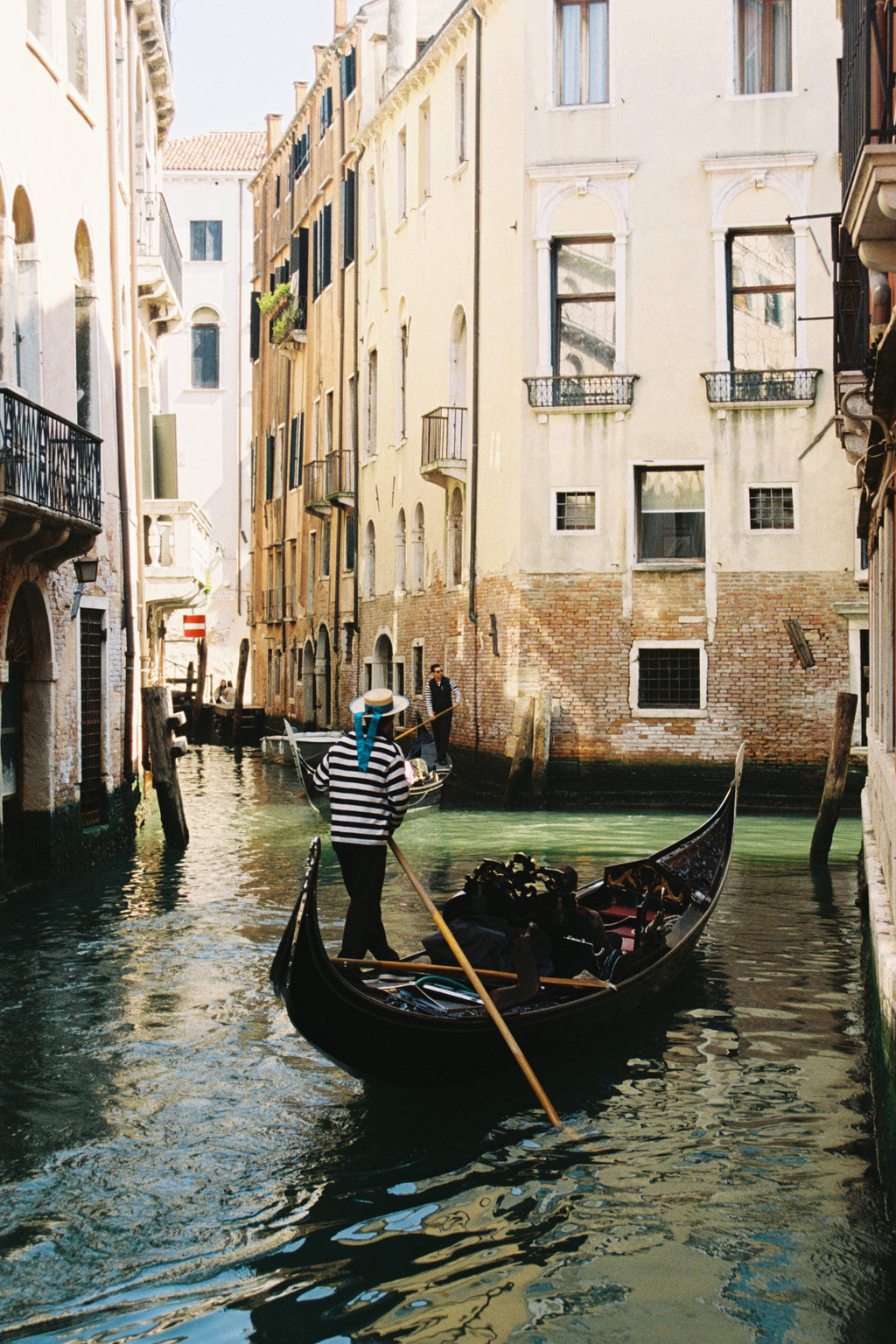 Gondolier in a gondola on a canal with buildings reflected in the water