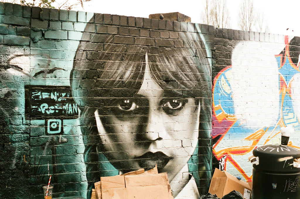 Mural of a woman's face on a brick wall with colorful graffiti in the background.