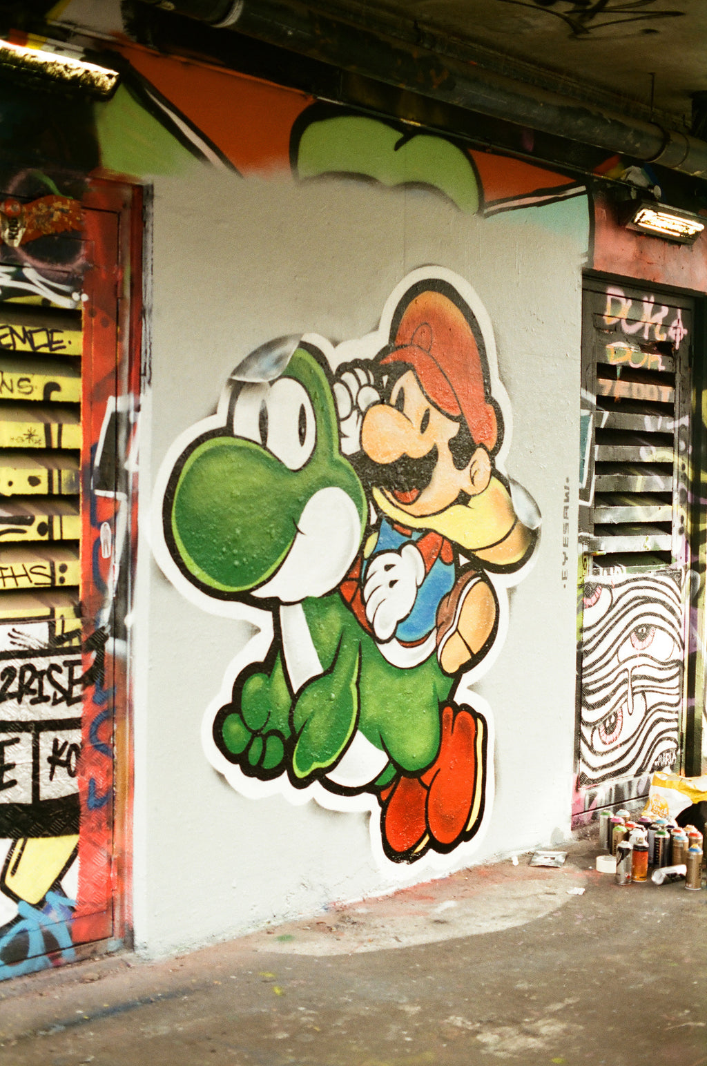 Cartoon character holding a green creature on a wall with graffiti.